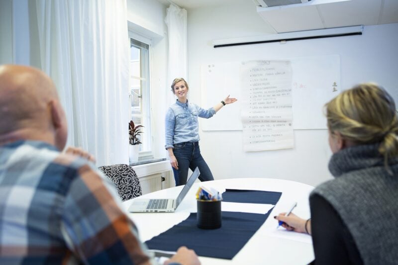 En av Misa Uppsalas arbetskonsulenter pekar på en whiteboard och talar till två åhörare vid ett konferensbord